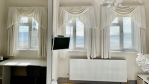 A room with a desk, chair, and a view of the sea through large windows with white curtains. - The Waterfront Inn (Shanklin)