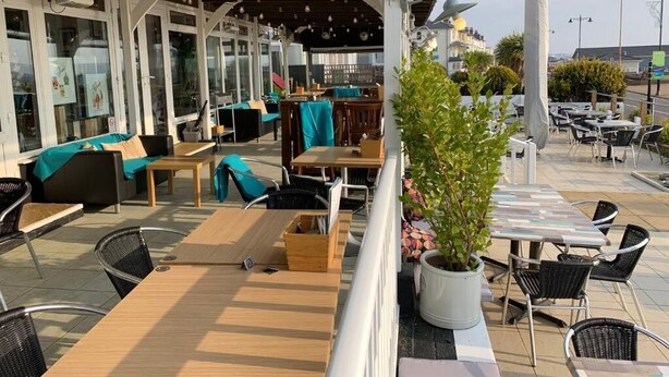 An outdoor seating area with tables and chairs, a potted plant, and a covered section with a view.