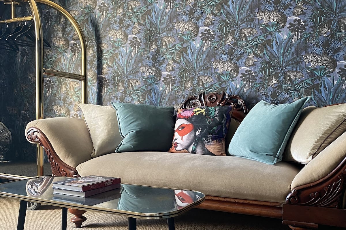 A cozy living room with a sofa, a glass coffee table, and a patterned wallpaper.