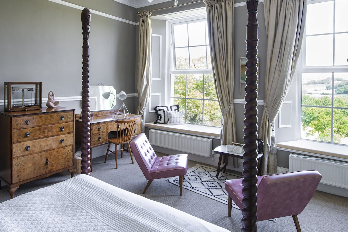 A bedroom with a four-poster bed, a wooden dresser, a desk, and a chair.