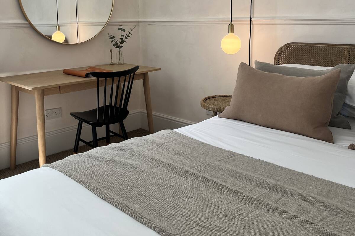 A bedroom with a bed, a desk, a chair, a round mirror, and a hanging light fixture.