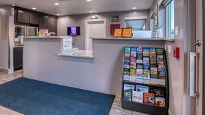 Una zona de recepció amb un rellotge digital, un tauler d'anuncis amb fulletons turístics i una cuineta petita.