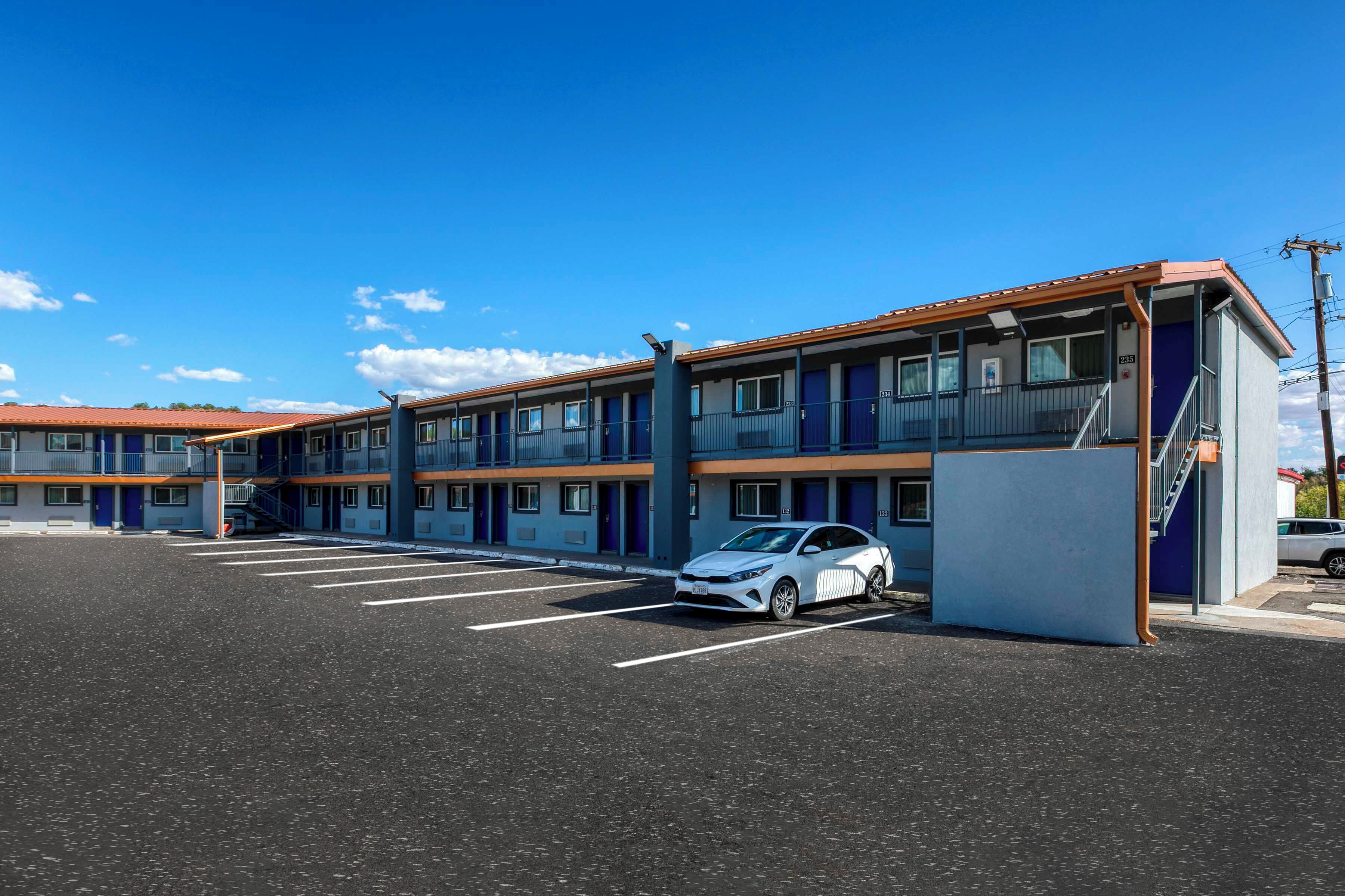 Ein Motel mit mehreren Zimmern, einem Parkplatz und einem davor stehenden Auto.
