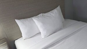 Un llit ben fet amb llençols i almoades blanques, un reposacapses de fusta i una paret sense decoració.