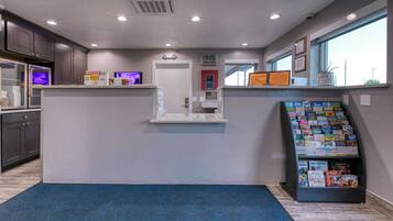 A reception area with a counter, a digital kiosk, a magazine rack, and a door leading to a hallway.