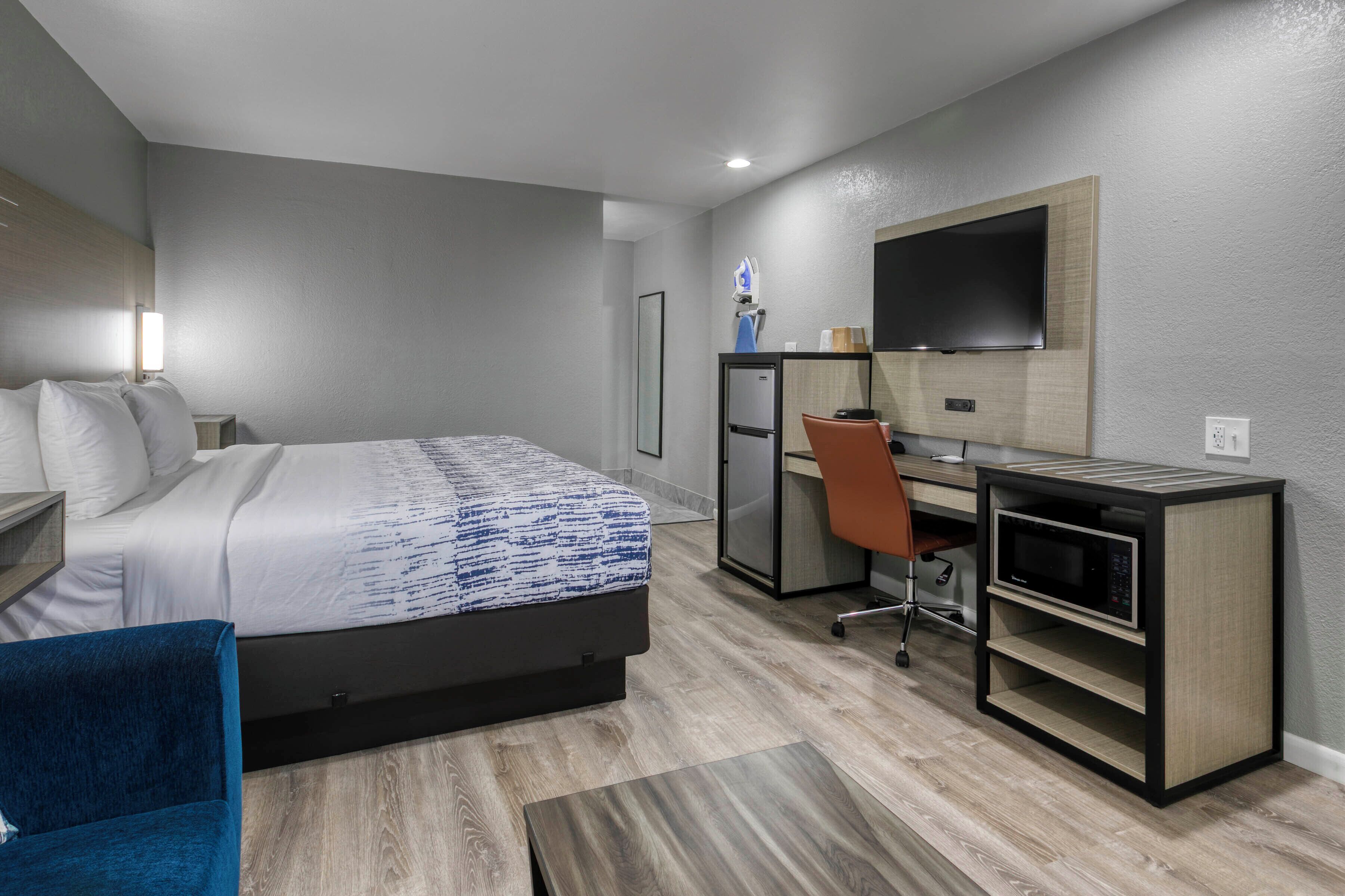 A hotel room with a bed, desk, chair, television, and a microwave.