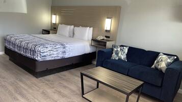 A hotel room with a bed, a sofa, a coffee table, and a nightstand with a phone.