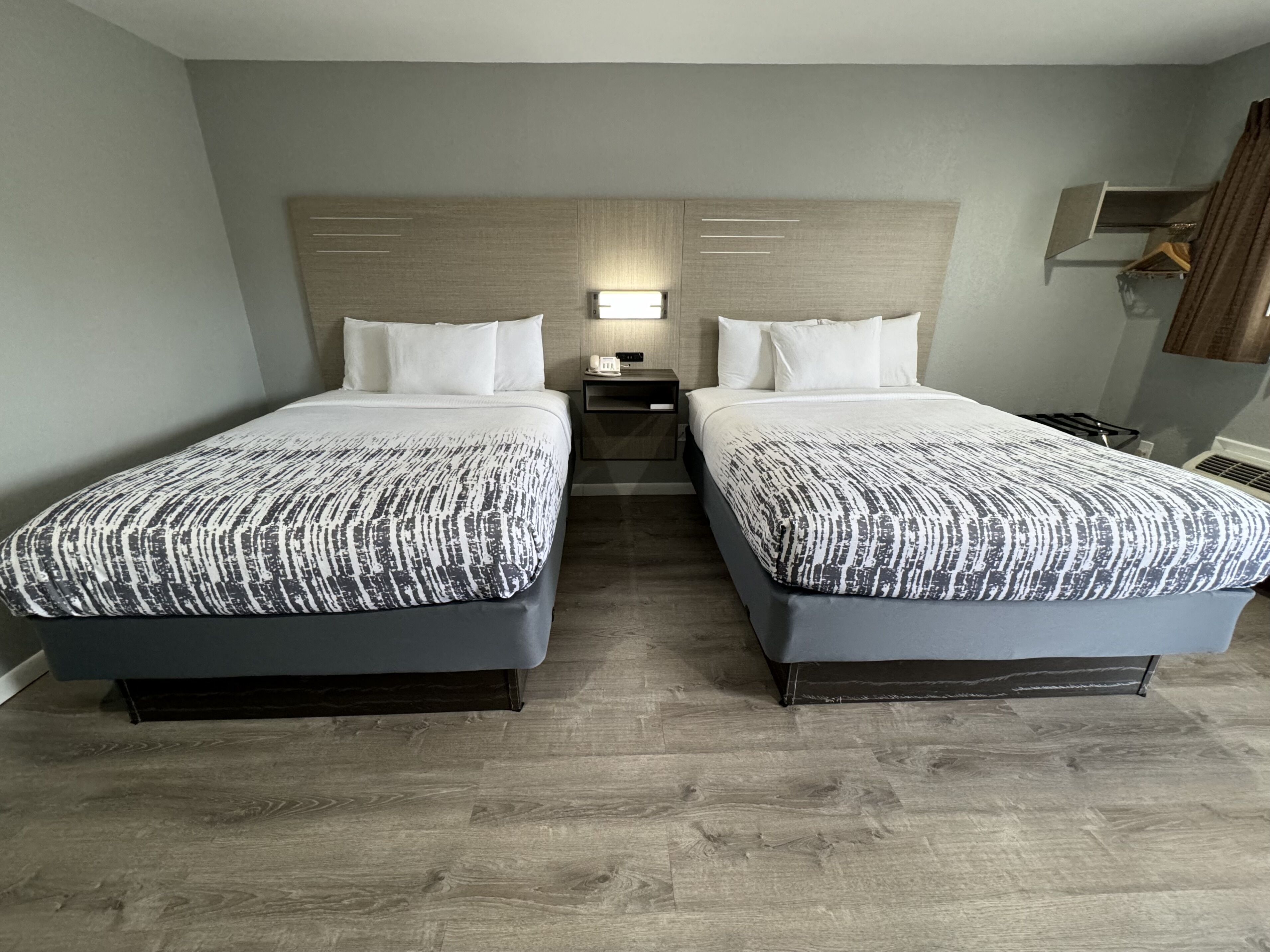 Una habitación de hotel con dos camas, una mesita de noche, una lámpara y un armario.