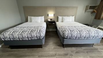 Una habitación de hotel con dos camas, una mesita de noche, una lámpara y un armario.