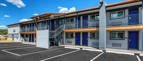 Un motel con una estructura de dos pisos, un área de estacionamiento techada y una escalera al nivel superior.