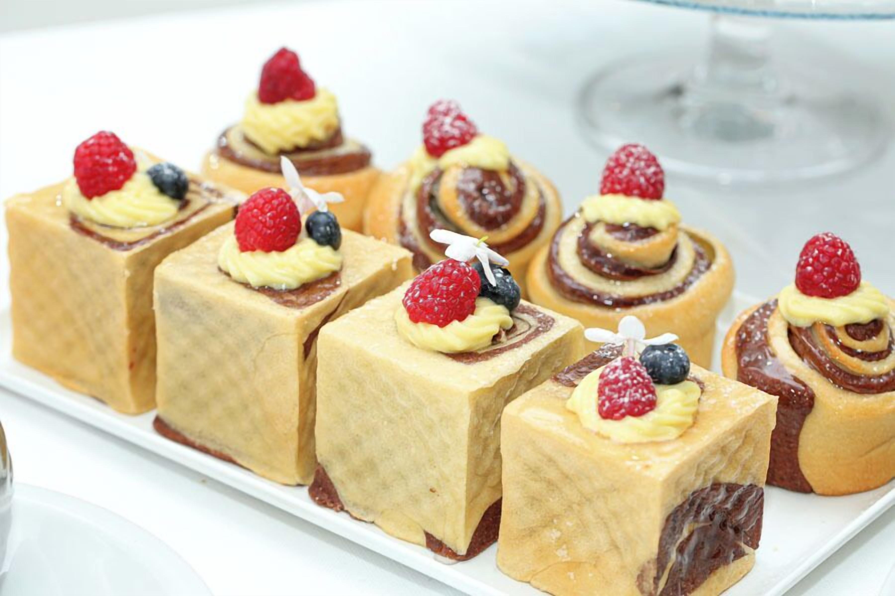 Variedad de postres en un plato blanco, incluyendo pasteles cuadrados y redondos con frutas.