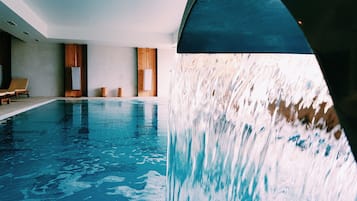 Una piscina interior con caída de agua, sillones de madera para relajarse y un diseño de interiores moderno.
