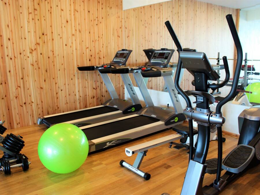 Un gimnasio con cintas de correr, una máquina elíptica y una pelota de ejercicios verde.