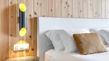 Quarto com painel de parede de madeira, mesa de cabeceira com abajur, cama com roupa de cama e almofadas brancas, e uma tomada na parede.