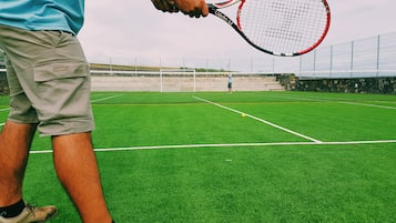 Un court de tennis avec un filet, un joueur en arrière-plan et une personne tenant une raquette de tennis.