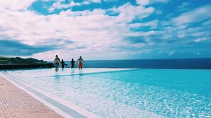 A pool with clear blue water, a stone wall, and a view of the ocean and sky. - Pedras do Mar Resort & SPA (Ponta Delgada)