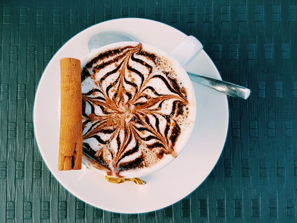 A white cup of coffee with latte art on a white plate, placed on a textured surface. - Pedras do Mar Resort & SPA (Ponta Delgada)