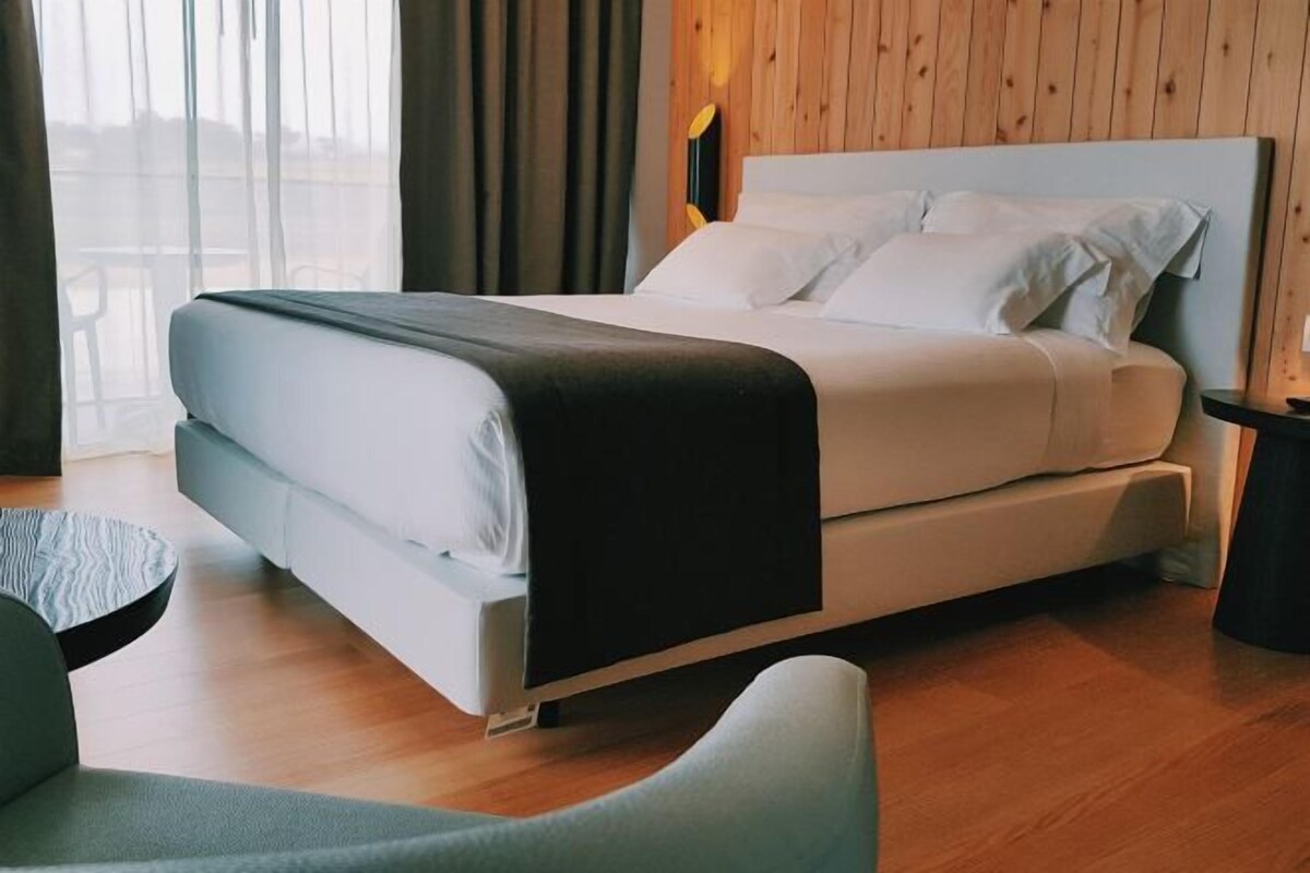 A modern hotel room with a bed, a chair, and a wooden floor.