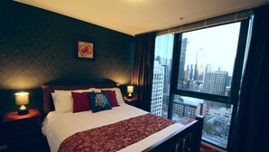 Ein Hotelzimmer mit einem großen Bett, zwei Nachttischlampen, Blick auf die Stadt und einem gerahmten Kunstwerk an der Wand.