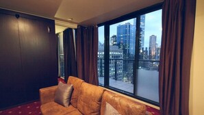 Ein Zimmer mit großem Fenster, einem braunen Ledersofa und Blick auf eine Stadtlandschaft.