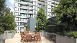 Ein Innenhof mit einem runden Holztisch und Stühlen, umgeben von Pflanzkästen und Bänken.