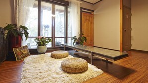 A room with a large window, wooden flooring, a glass table, and two woven poufs. - Jiwoljang Guest House (Seoul)