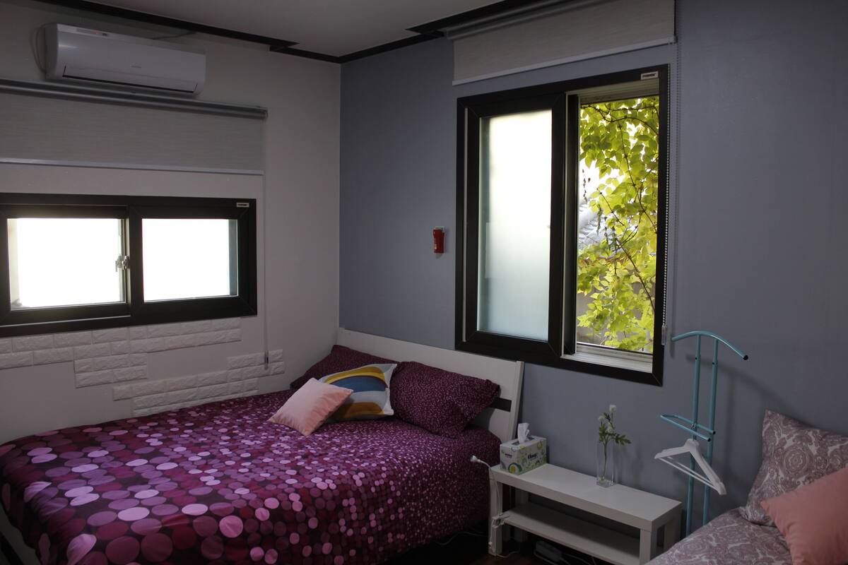 Een slaapkamer met een bed, nachtkastje, raam en een airconditioning.