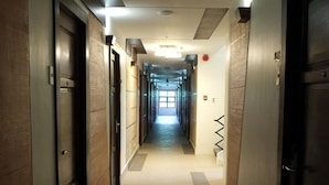 Un largo pasillo de hotel, estrecho, con puertas a ambos lados, suelo de baldosas e iluminación empotrada en el techo.