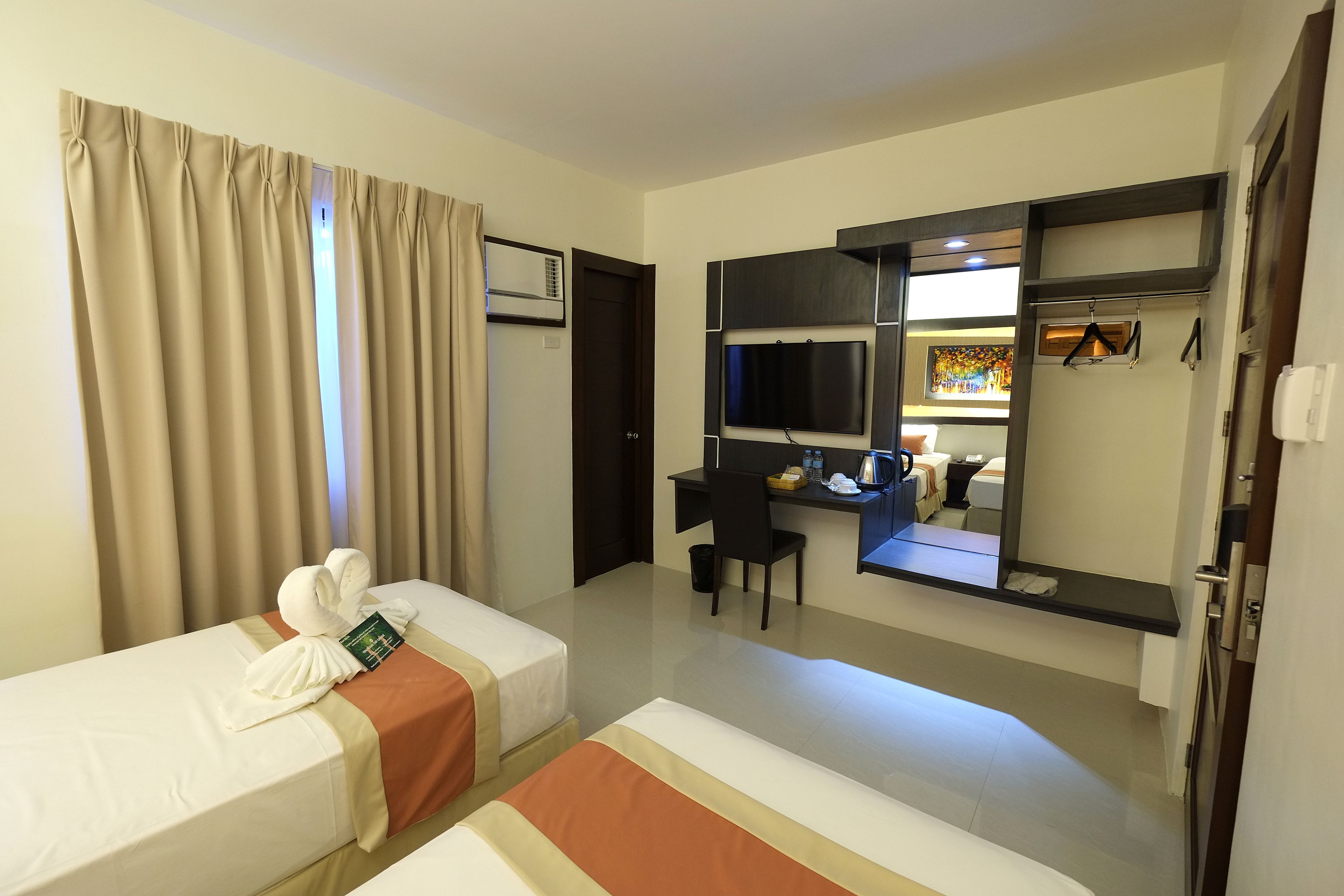A hotel room with two beds, a desk, a chair, a TV, and a mirror.