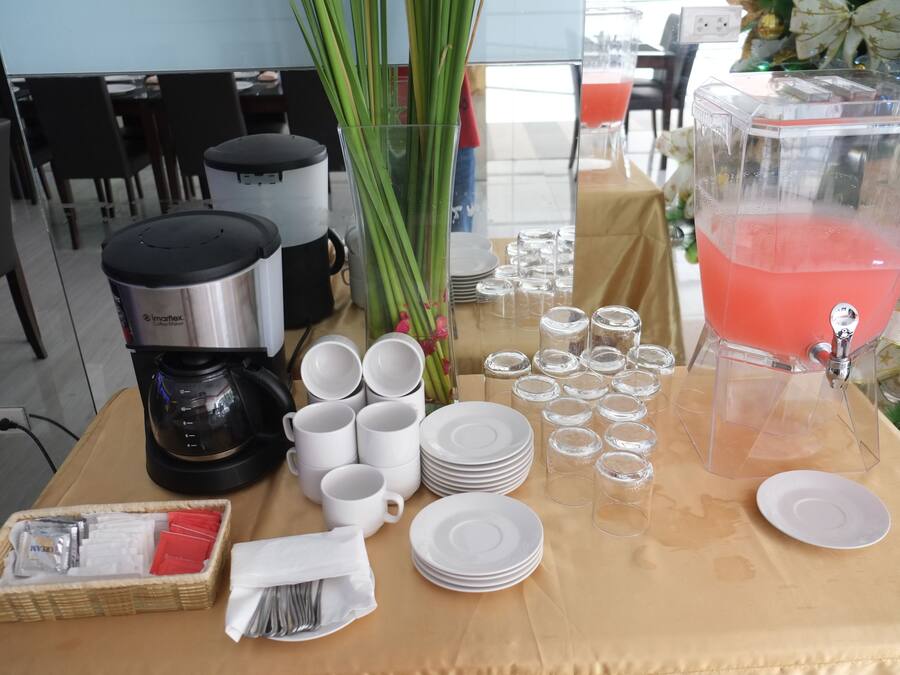 A breakfast setup with coffee maker, cups, plates, and a punch dispenser.