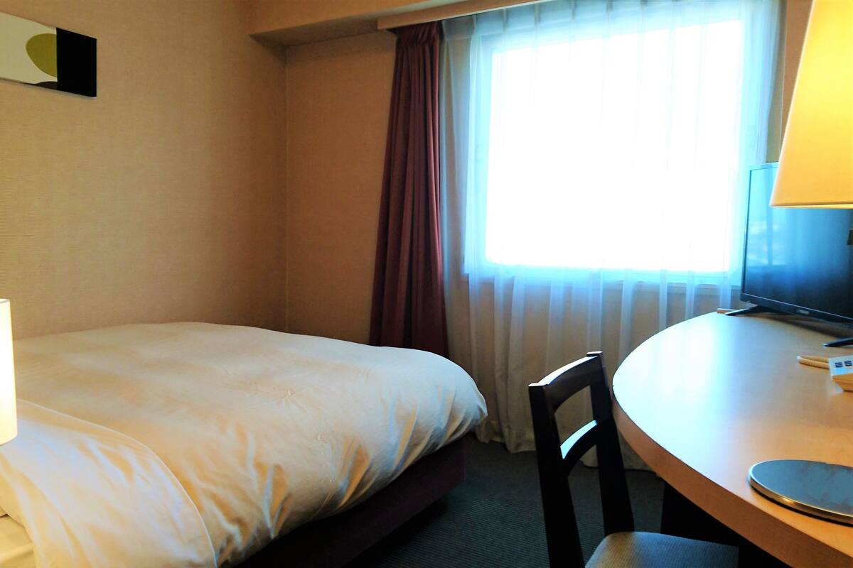 Habitació d'hotel amb un llit, escriptori amb làmpada, una cadira i televisió.