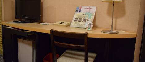 A hotel desk with a television, a lamp, a chair, a trash bin, and a brochure on the desk.