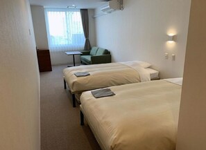 Habitación de hotel con dos camas, una mesita, una silla y una ventana con cortinas.