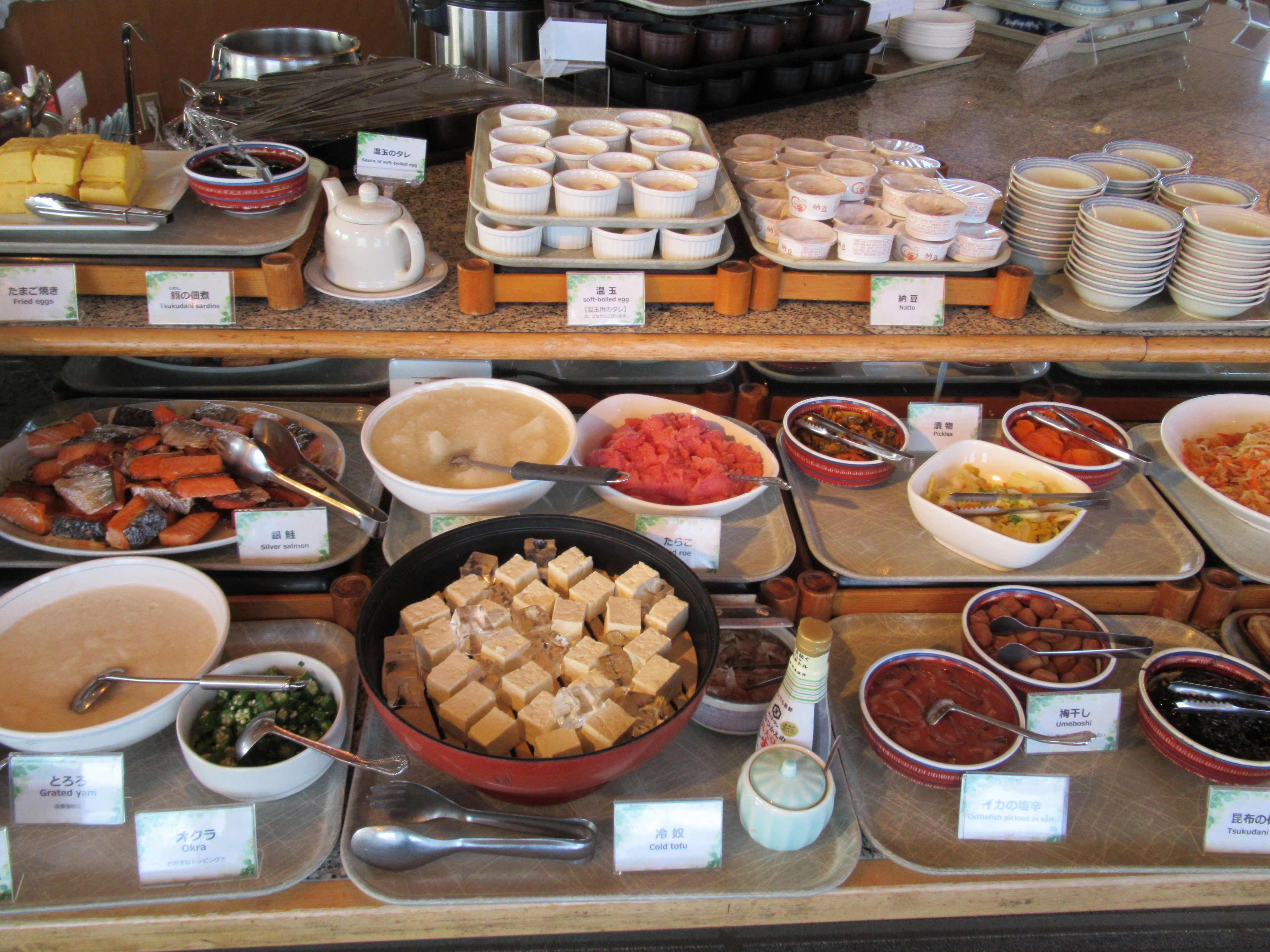 Een buffet met diverse gerechten, waaronder tofu, augurken en verschillende soorten soep.