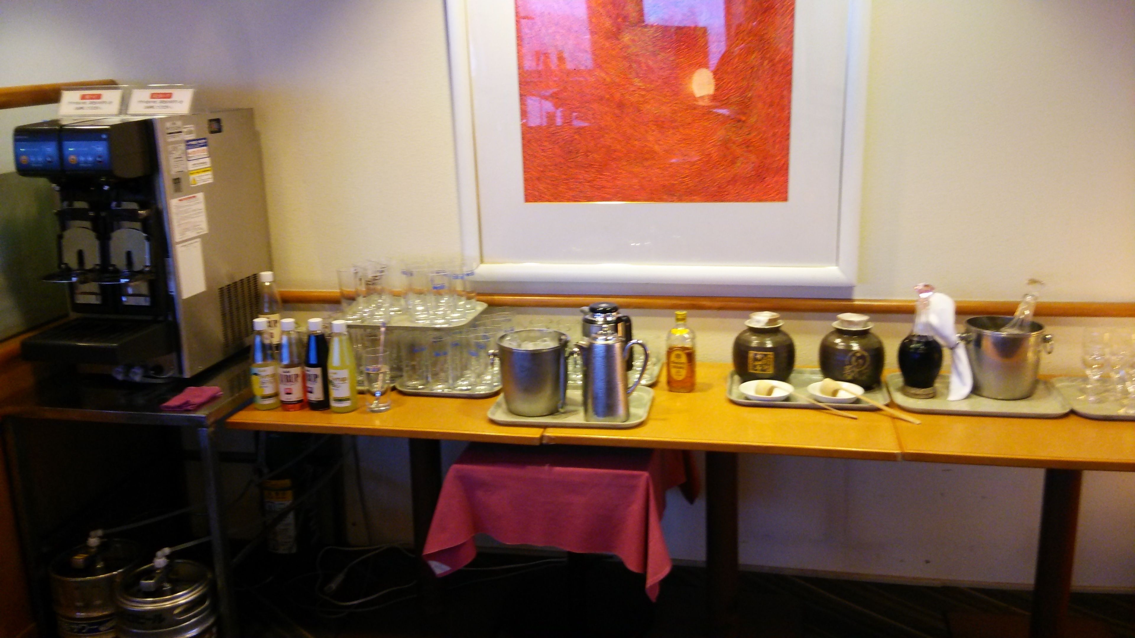 A bar area with a coffee machine, various bottles, glasses, and a framed artwork on the wall.