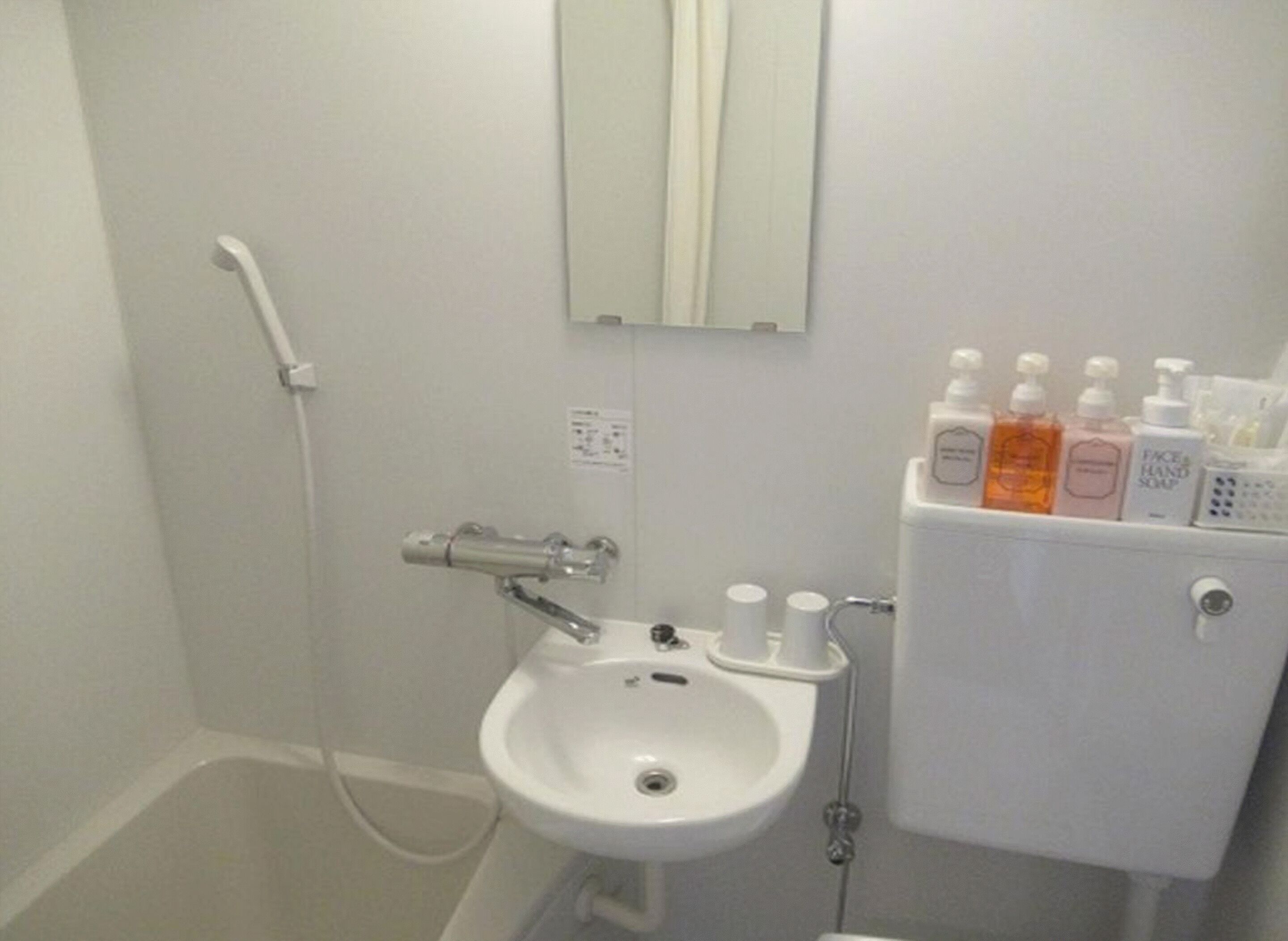 A bathroom with a white sink, a mirror above it, and a toilet with toiletries on top.
