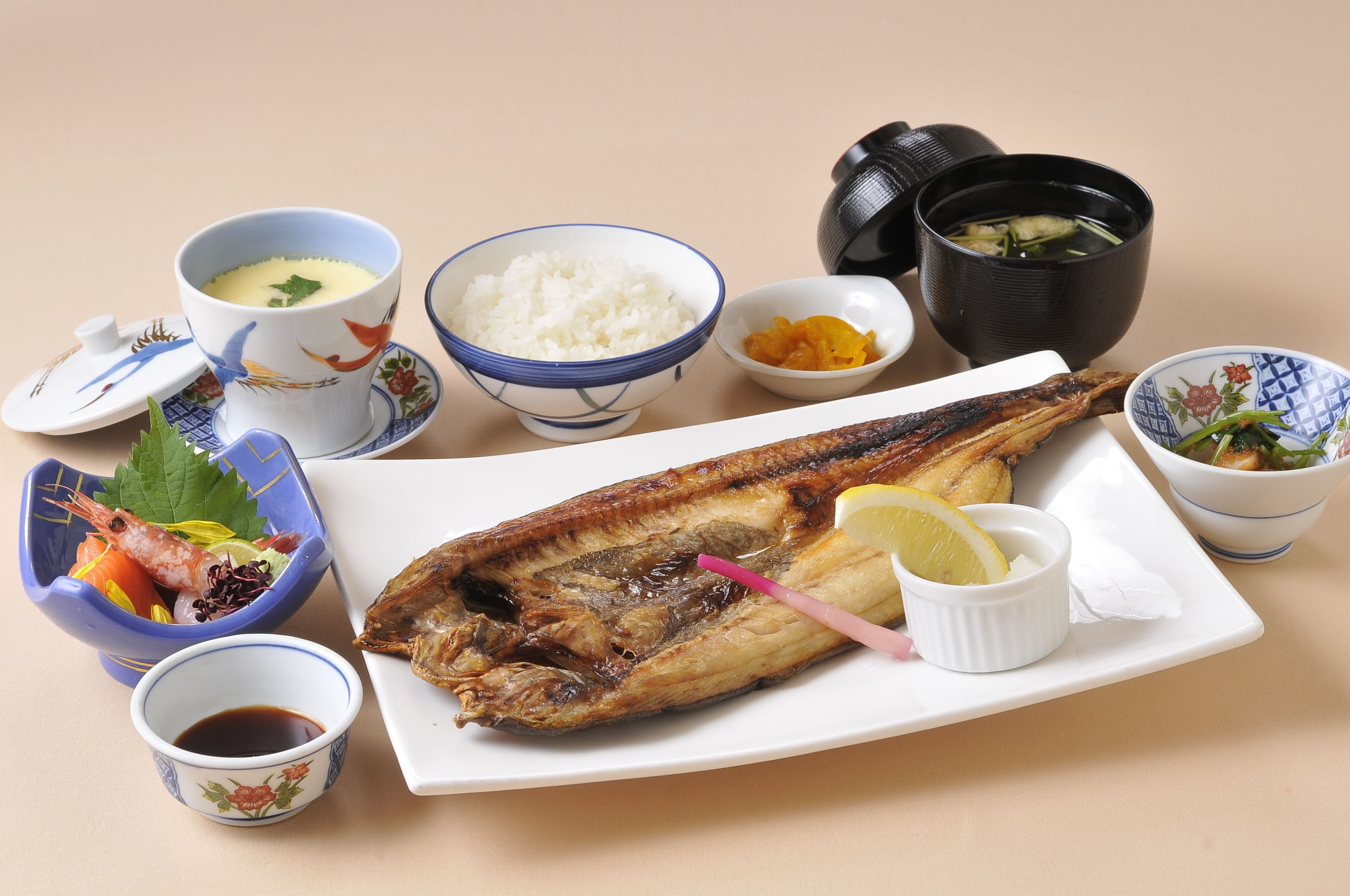 A meal with a whole grilled fish, rice, and various side dishes.