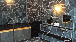 Un baño con pared de piedra, una bañera negra y un lavamanos negro con espejo.