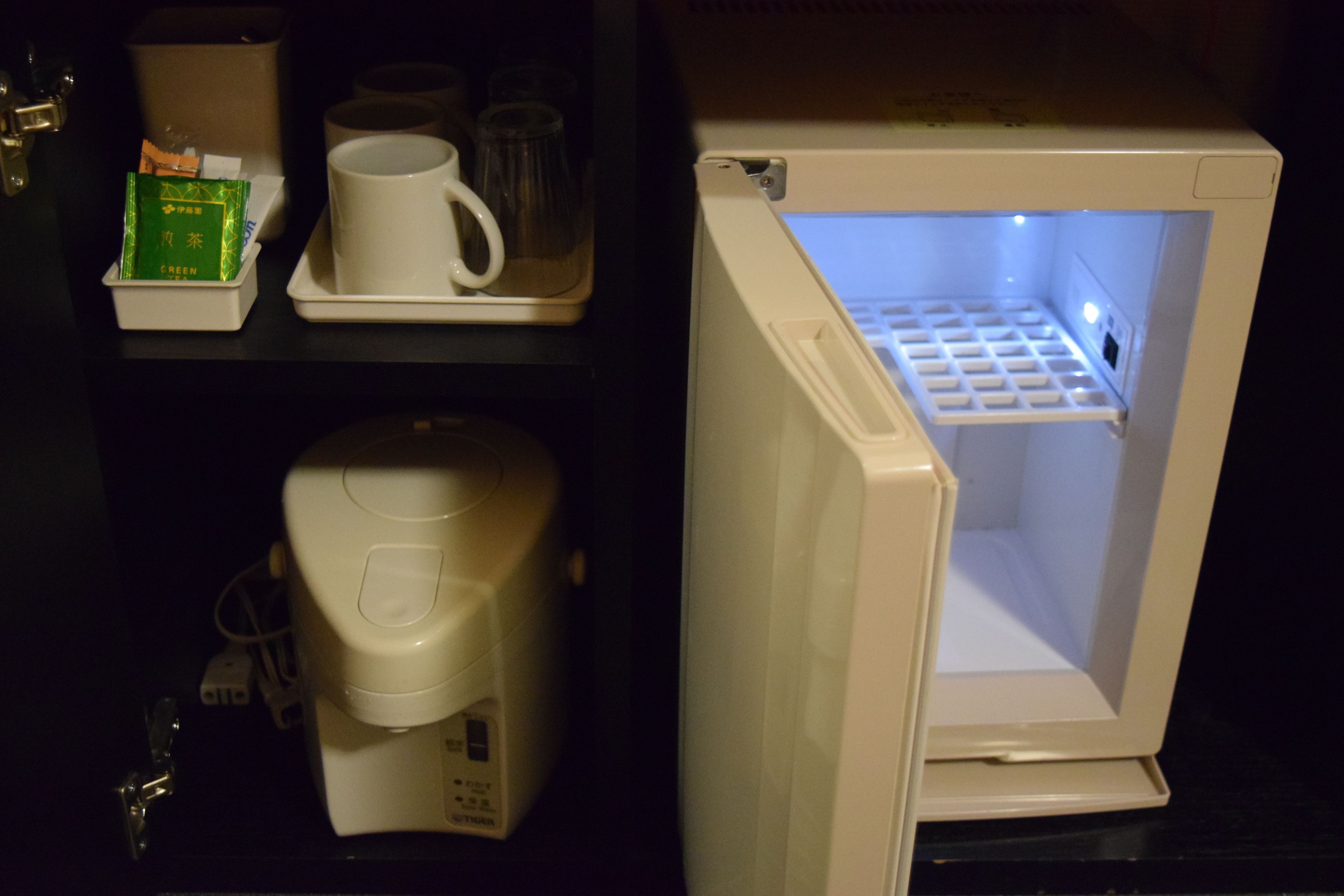 A compact refrigerator with a freezer compartment, a coffee maker, and a tray with a mug and a green box.