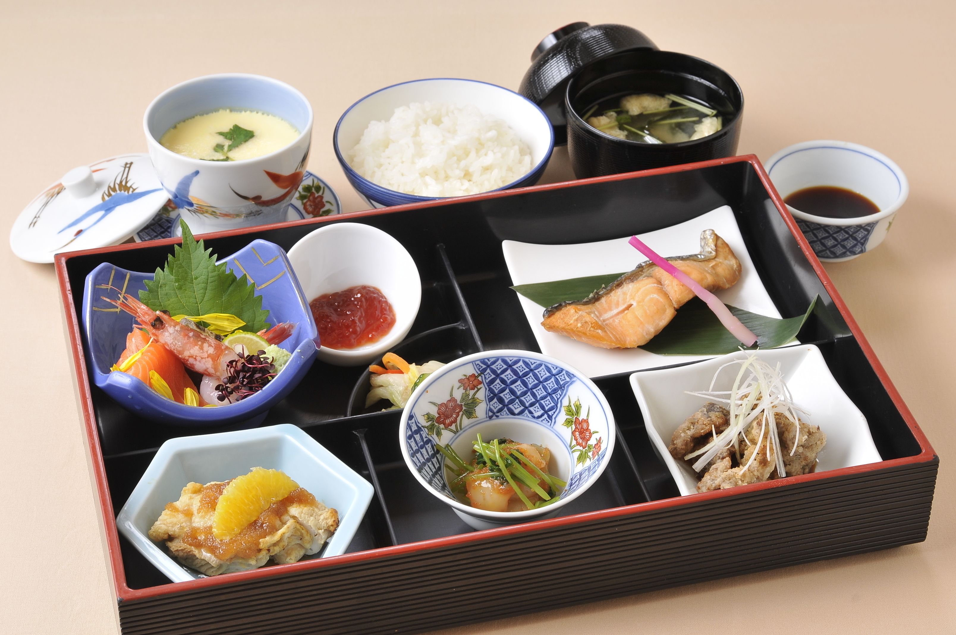 En traditionell japansk måltid serverad på ett svart bricka, med olika rätter som ris, fisk och grönsaker.