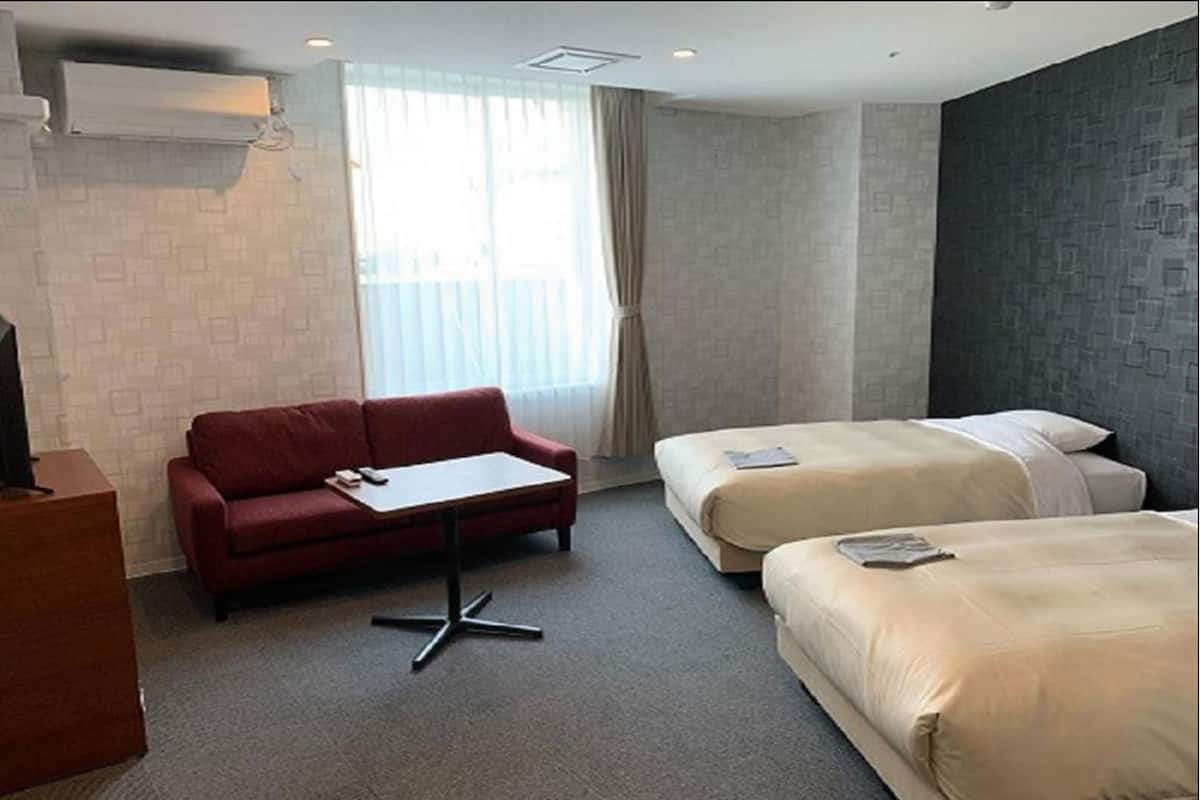 Habitació d'hotel amb un sofà vermell, dos llits individuals, una taula petita i un televisor.