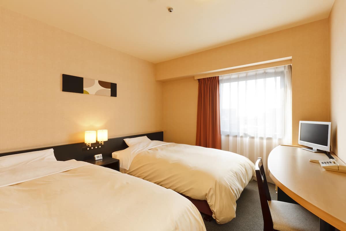 Habitació d'hotel amb dos llits, una escriptori, televisió i una finestra amb cortines.