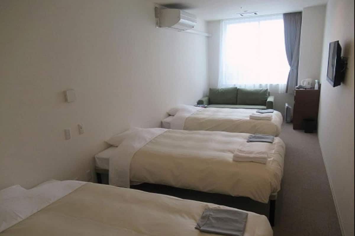 Habitació d'hotel amb tres llits, una finestra amb cortines, un televisió de pantalla plana i una taula petita amb una cadira.