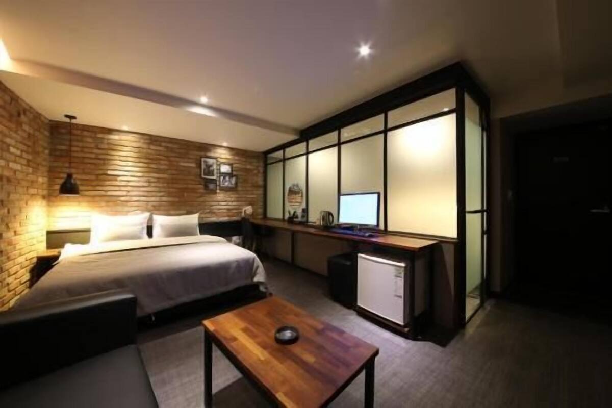 A hotel room with a bed, a desk, a computer, and a small refrigerator.