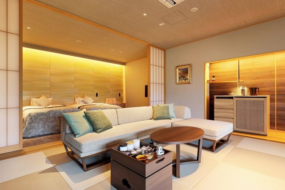 A modern hotel room with a sofa, a small table, a bed, and a kitchenette.