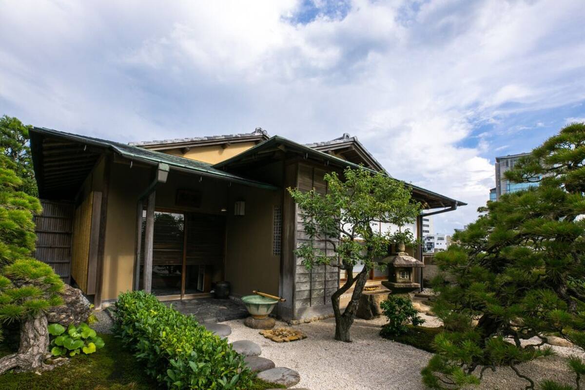 A traditional Japanese building with a covered entrance, a stone lantern, and a well-maintained garden with rocks and greenery.