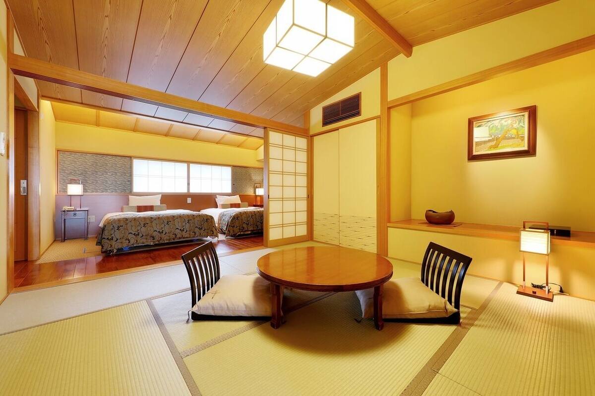 A traditional Japanese-style room with tatami flooring, a low table with cushions, and a bed with a floral-patterned bedspread.