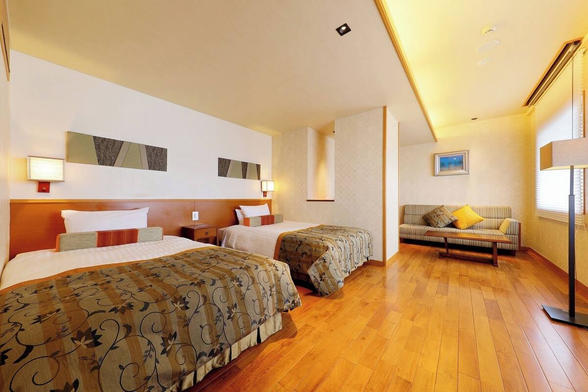 A hotel room with two beds, a sofa, a lamp, and artwork on the walls.
