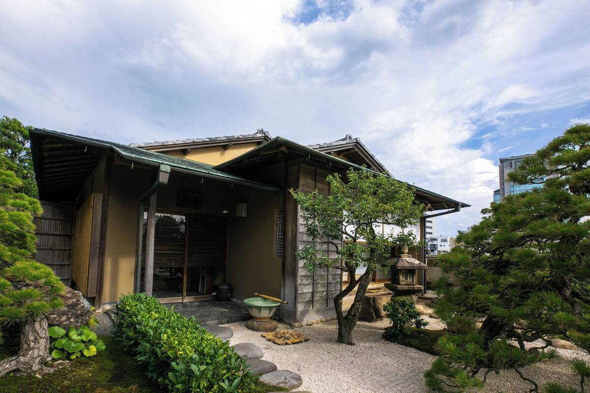 A traditional Japanese building with a covered entrance, a stone pathway, and surrounding greenery.