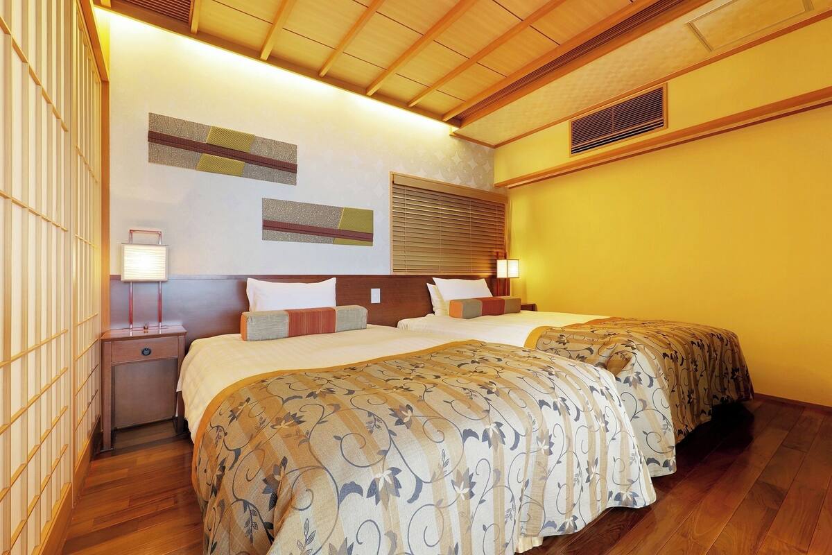 A hotel room with a wooden ceiling, a bed with a patterned bedspread, a bedside table with a lamp, and a wall with decorative panels.
